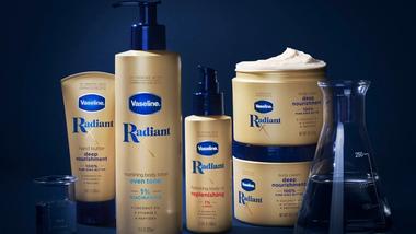 Products from Vaseline’s Radiant X collection, including Nourishing Body Lotion and Hydrating Body Oil. Packaging is golden on a dark blue background.