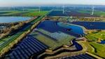 Aerial view of a vast solar panel farm followed by a wind farm among fields and lakes