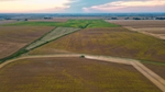 A bird's eye view of vast farm land and an open sky. A truck makes its way down the middle of the view.